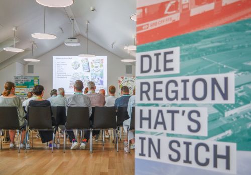 Saal mit Menschen, Fokus auf Banner mit der neuen Kampagnenphase 4